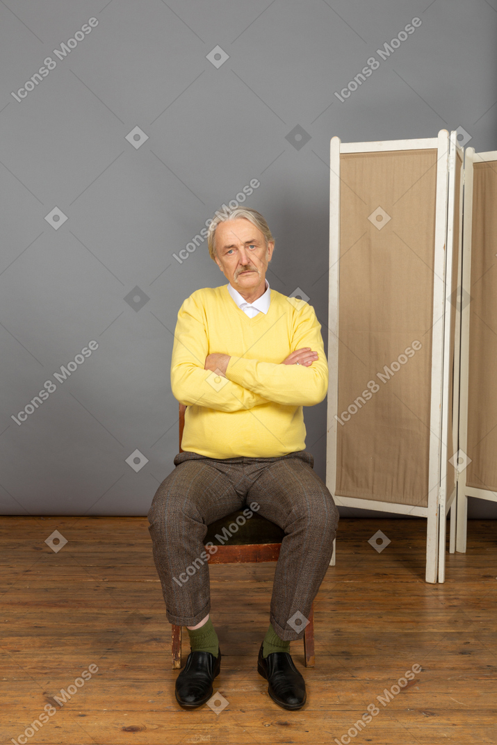 Serious-looking man sitting in chair with crossed arms