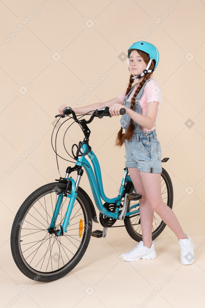 Teenage girl in blue helmet standing near blue bicycle