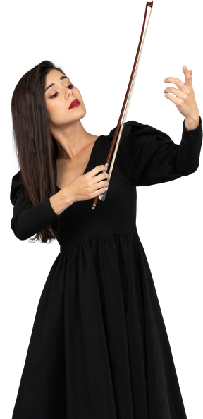 Vista frontal de uma jovem de vestido preto impressionando ao tocar violino