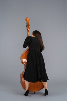 Vista posterior de un joven músico en vestido negro sosteniendo su contrabajo