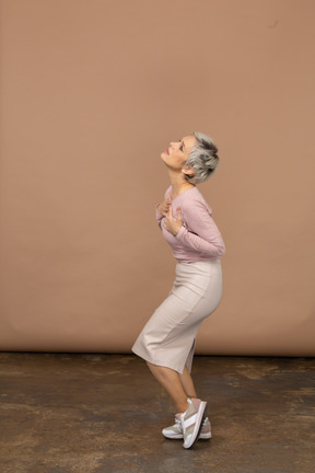 Vista lateral de uma mulher emocional em roupas casuais em pé com as mãos no peito