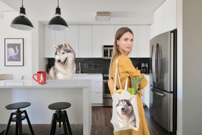 A woman with a bag of groceries coming home to her dog