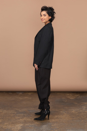 Vista lateral de una empresaria vistiendo traje negro y mirando a la cámara