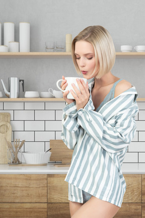 A woman in striped pajamas drinking coffee in the kitchen