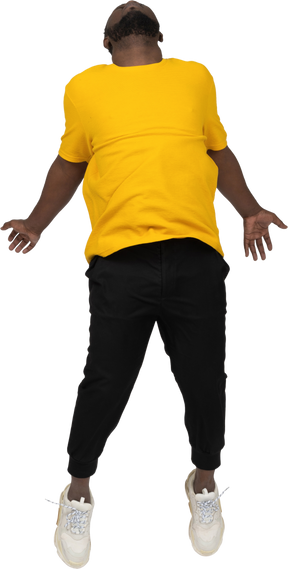 Vista frontal de um jovem de pele escura pulando em uma camiseta amarela estendendo as mãos