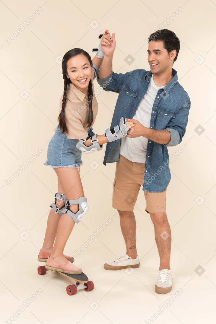 Chico caucásico joven enseñando a chica asiática a patinar