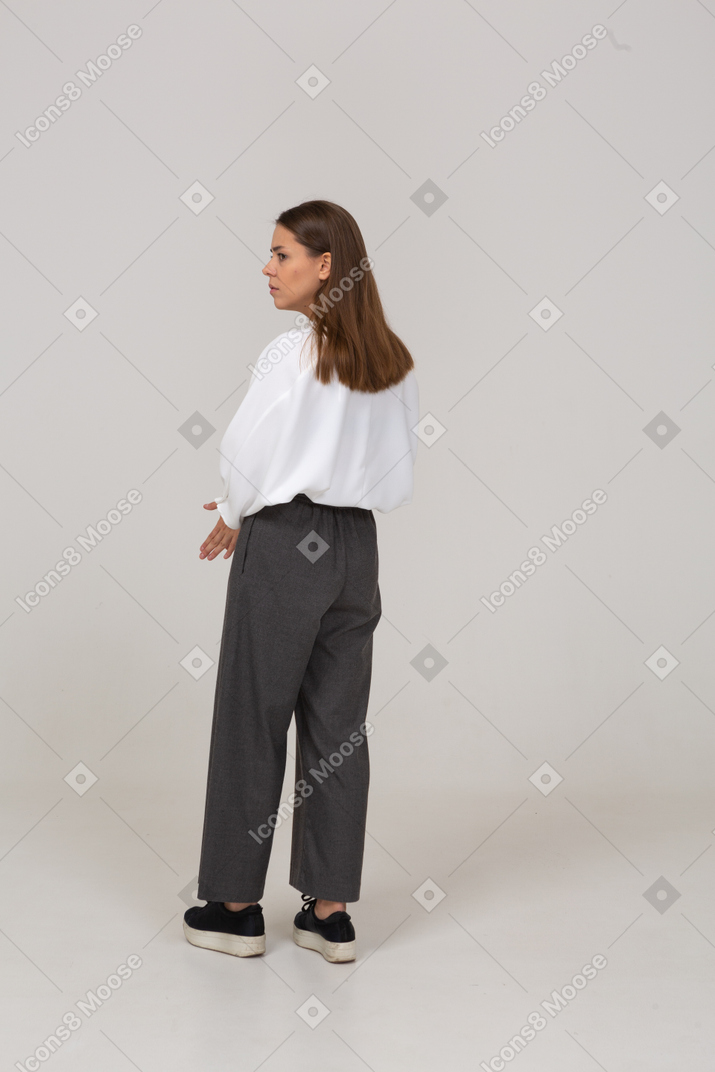 Three-quarter back view of a thoughtful young lady in office clothing looking aside