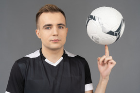 Vista frontal de un jugador de fútbol masculino mirando a la cámara y sosteniendo una pelota en su dedo