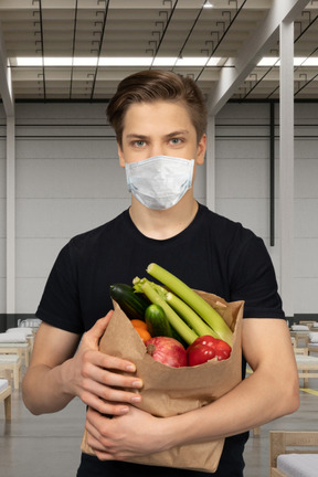 A man wearing a face mask holding a bag of vegetables