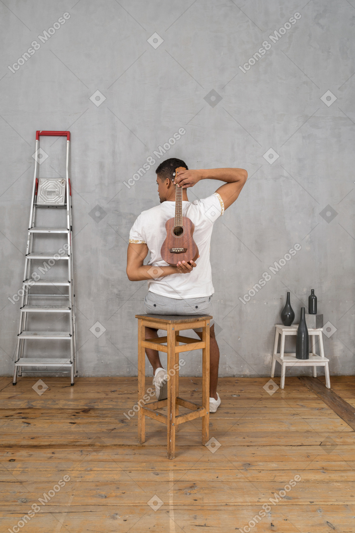 Vista posteriore di un uomo su uno sgabello che tiene un ukulele dietro la schiena