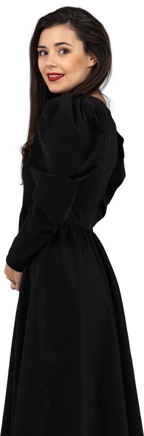 Vista lateral de una joven con un vestido negro de pie y mirando a la cámara