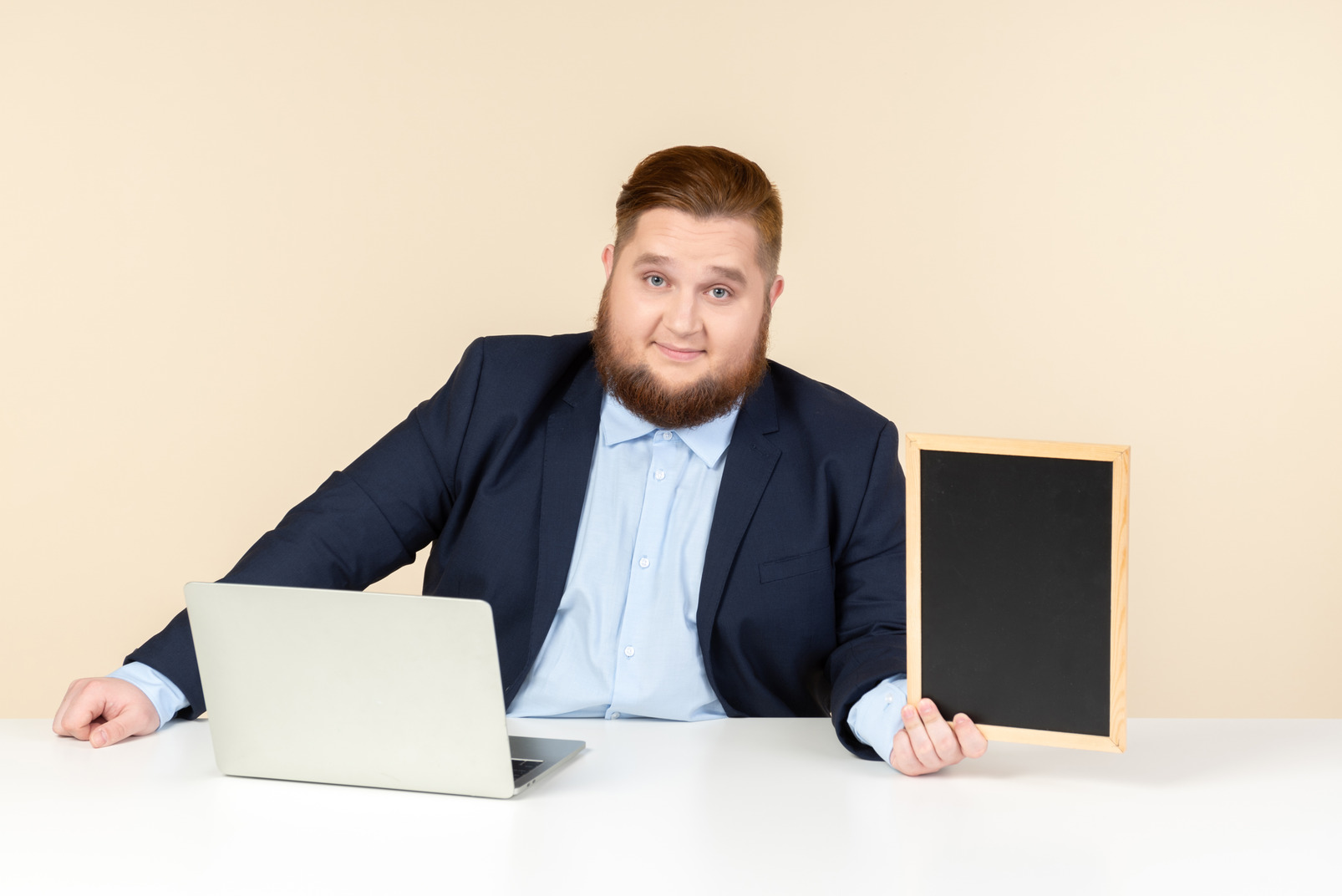 Young overweight man sitting in front of laptop and holding small blackboard