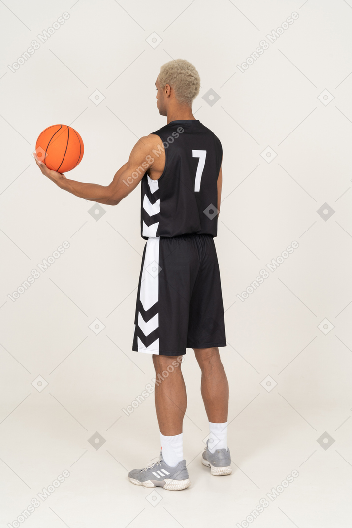 Vista posteriore di tre quarti di un giovane giocatore di basket maschile che tiene una palla