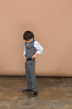 Vista frontal de un niño en traje de pie con las manos en el cinturón