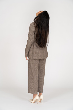 Three-quarter back view of a young lady in brown business suit throwing head back