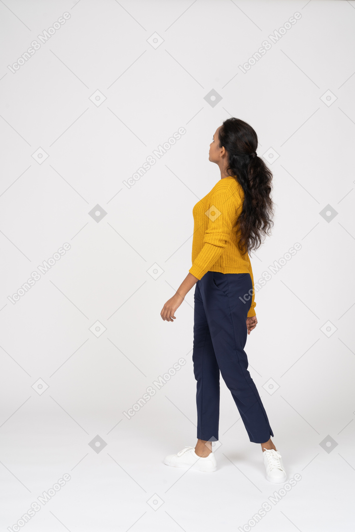 Vista laterale di una ragazza in abiti casual che cammina e guarda in alto