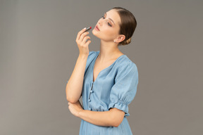 Vue de trois quarts d'une jeune femme en robe bleue tenant un rouge à lèvres