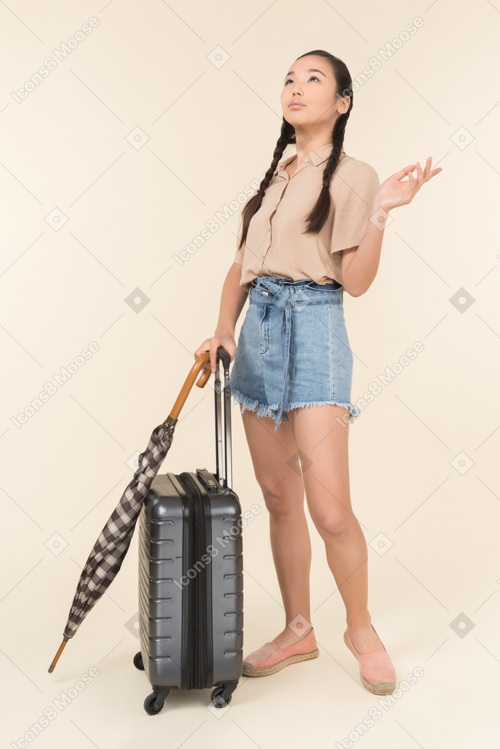Young woman with suitcase and umbrella looking up