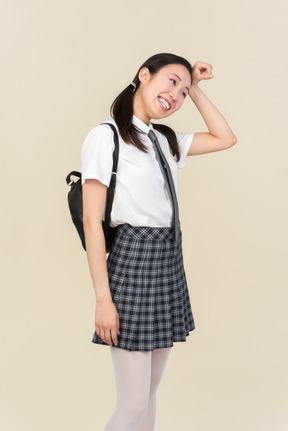 Asian school girl with backpack standing in profile and holding fist next to her forehead