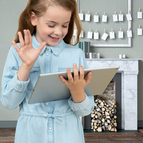 A little girl holding a tablet in front of a fireplace