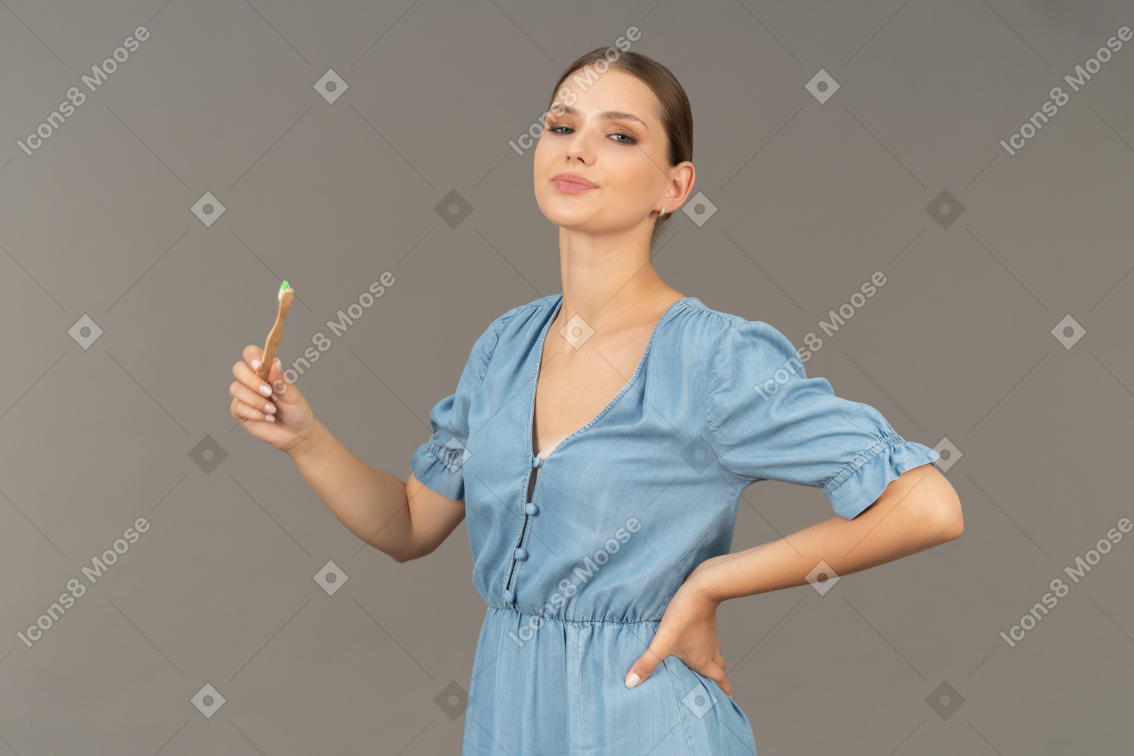 Three-quarter view of a proud young woman in blue dress holding a toothbrush