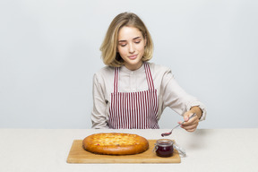 Mädchen am tisch sitzen und marmelade mit einem löffel nehmen