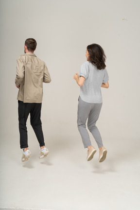 Three quarter back view of young man and woman jumping