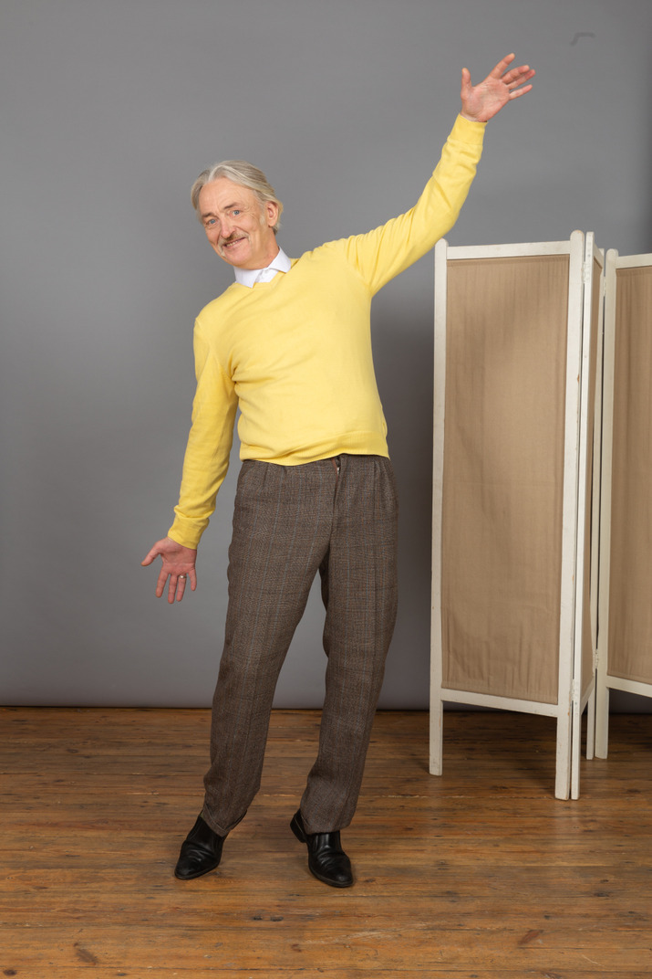 Three-quarter view of a smiling old man raising hand while leaning back