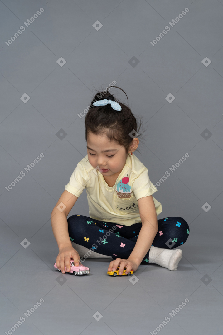 Little girl playing with toy cars while sitting on the floor