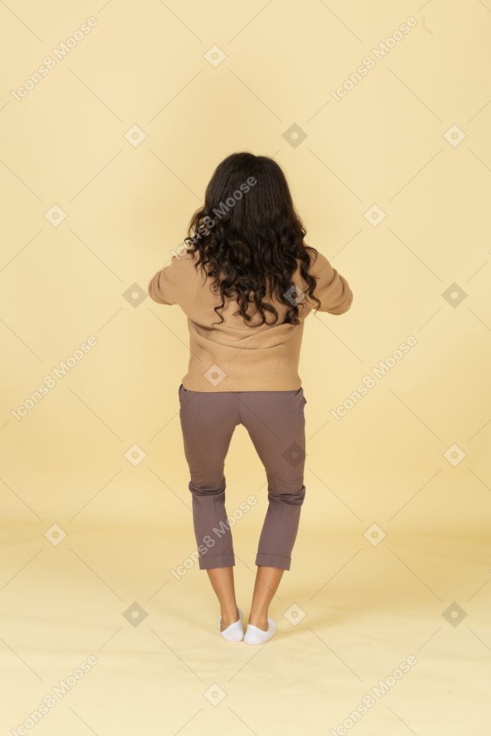 Back view of a squatting dark-skinned young female holding hands together