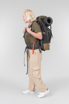 Mature female tourist standing in profile and carrying heavy backpack