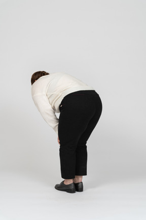 Rear view of a plump woman in white sweater bending down