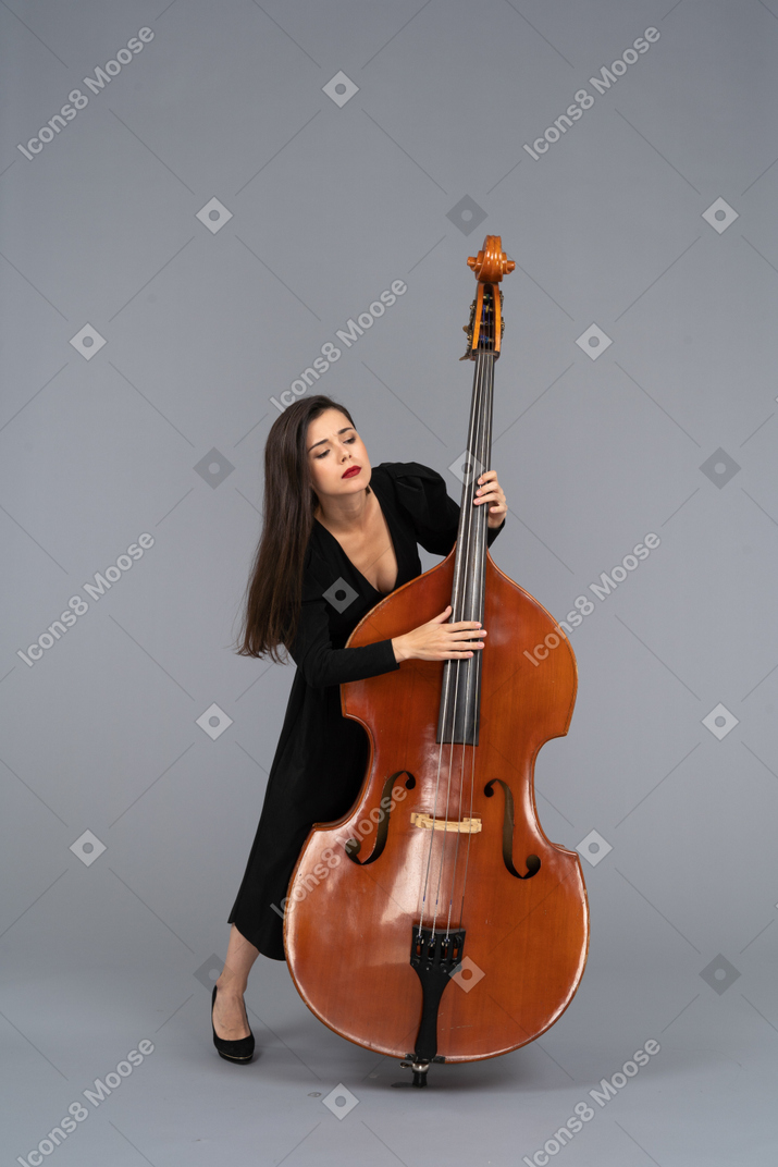Vista frontale di una giovane donna in abito nero che suona il contrabbasso e si sporge in avanti