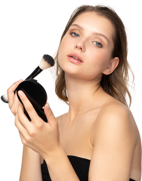 Vista lateral de una mujer joven que aplica polvos faciales mientras sostiene un espejo