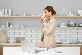 A woman sitting on a kitchen counter drinking from a mug