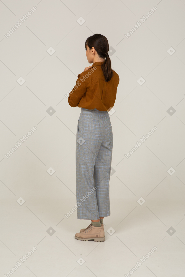 Three-quarter back view of a young asian female in breeches and blouse holding hands together