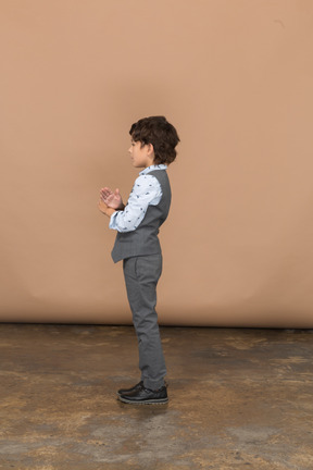 Vista lateral de un niño con traje gris que muestra un gesto de parada