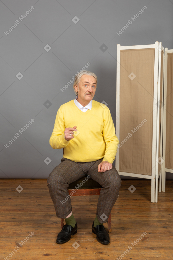 Мужчина средних лет сидит на стуле и смотрит в камеру