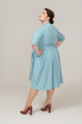 Side view of a woman in blue dress posing with hands on hips