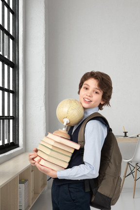 A boy holding a stack of books and a globe