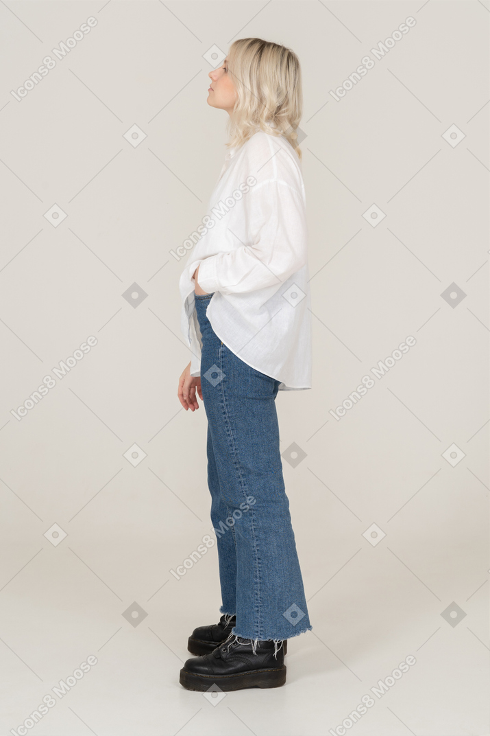 Side view of a blonde female in casual clothes putting hand in pocket and looking up