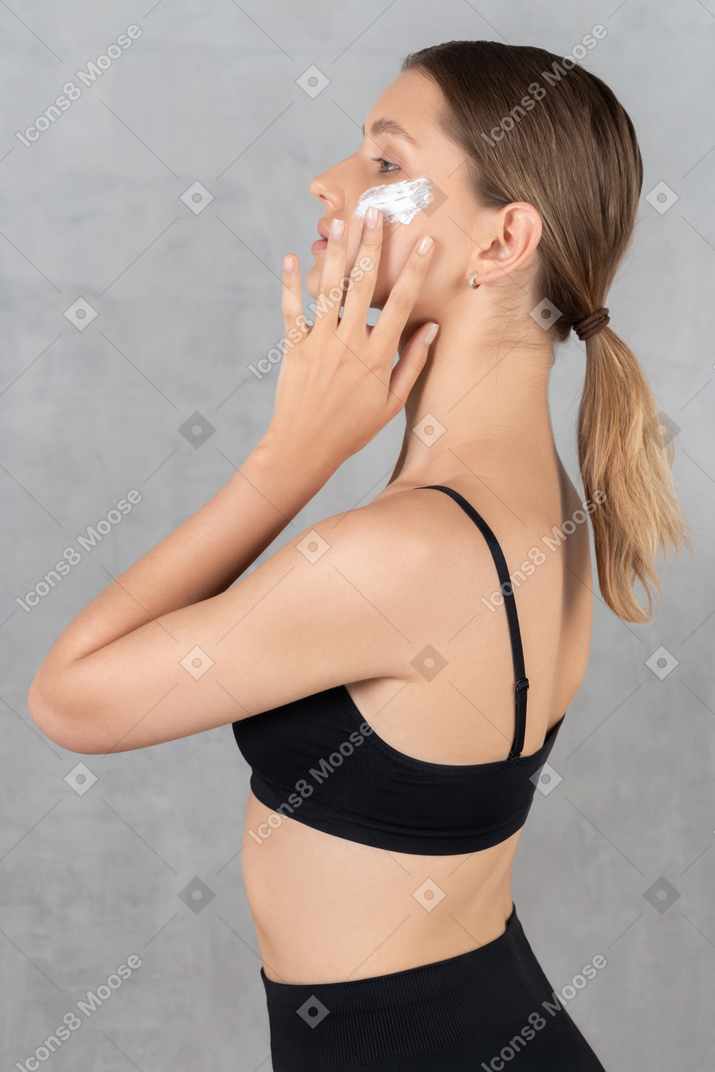 Side view of a young woman applying cream to cheekbones