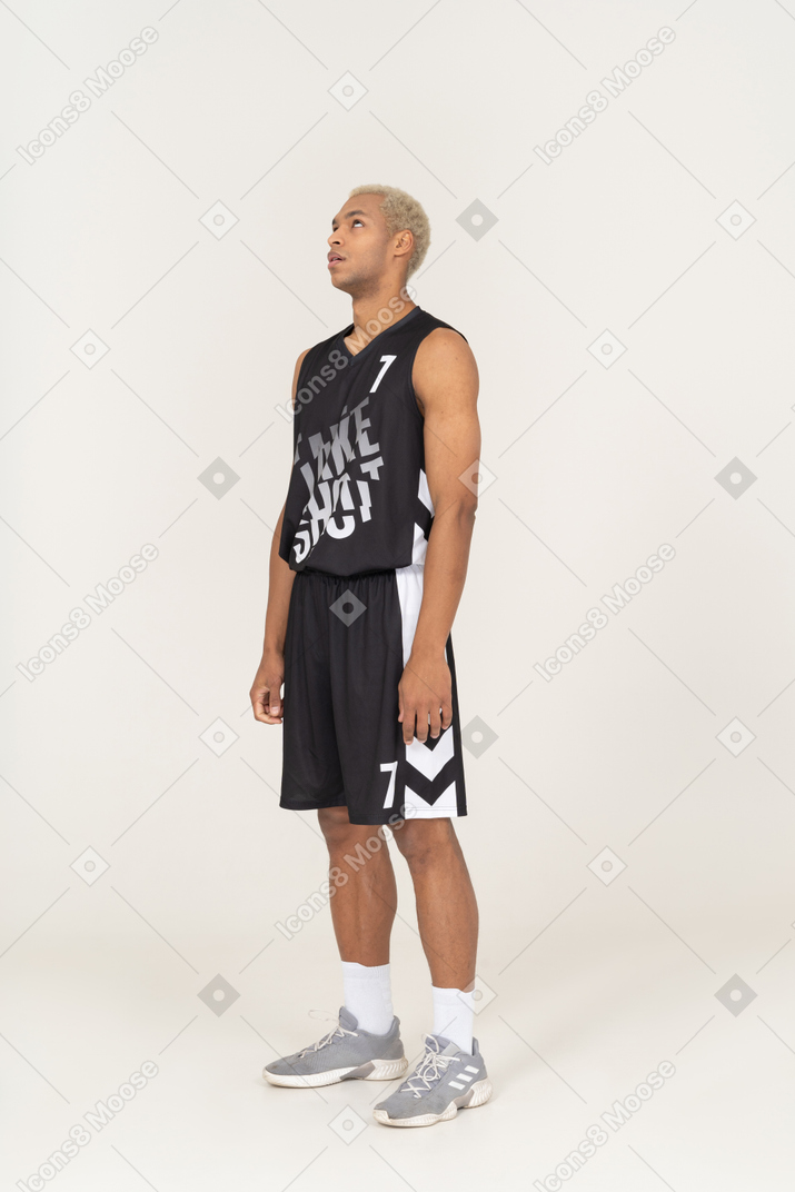 Vista de tres cuartos de un joven jugador de baloncesto masculino aburrido mirando hacia arriba