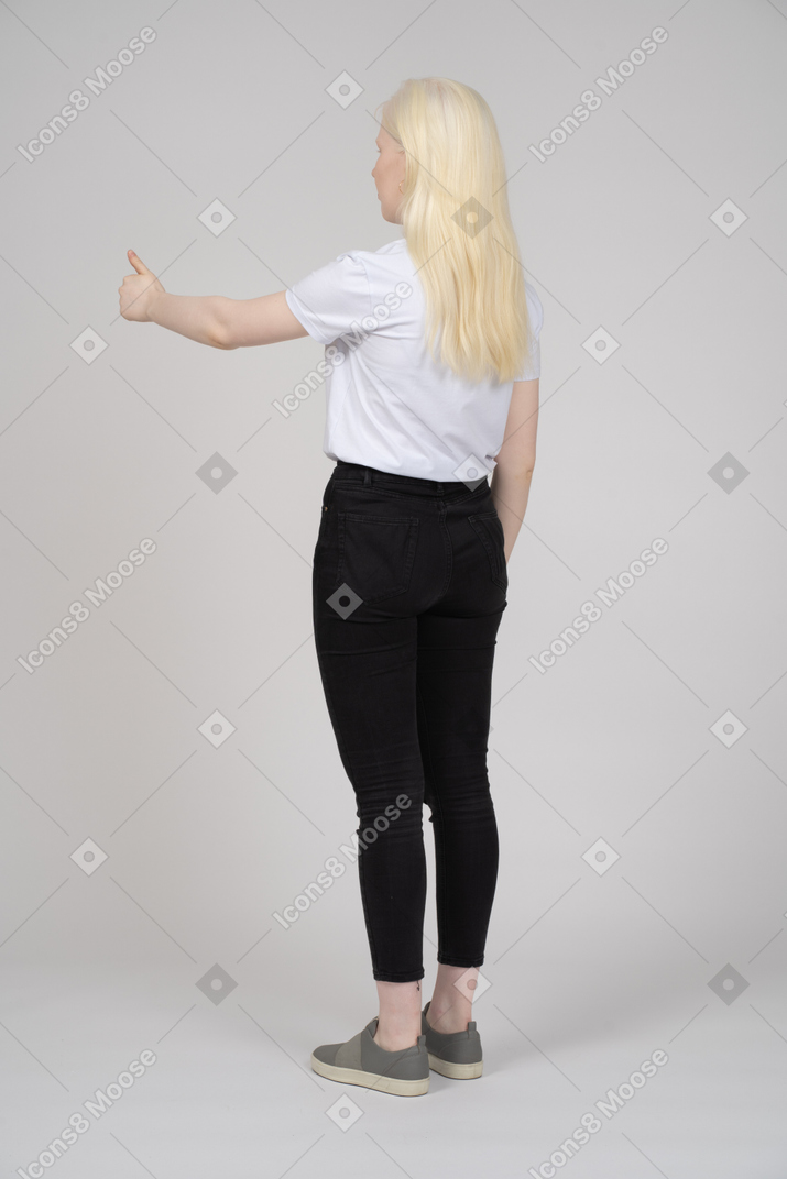 Вид сзади на молодую девушку, стоящую с поднятыми большими пальцами