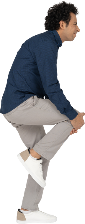 Vista laterale di un uomo in abiti casual che si tocca il ginocchio dolorante