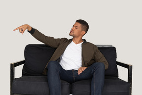 Вид спереди высокомерного молодого человека, сидящего на диване и держащего во рту сигарету