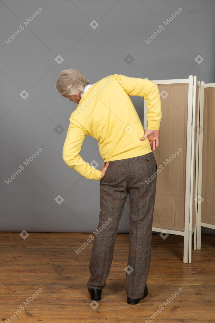 Back view of an old man putting hands on hips while leaning aside