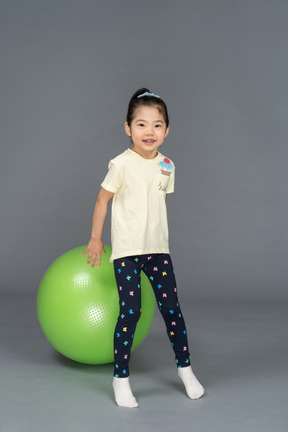 Petite fille debout devant un fitball vert