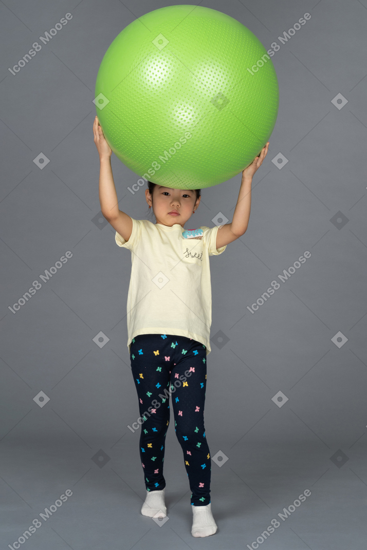 Kleines mädchen, das einen grünen fitball über ihrem kopf hält