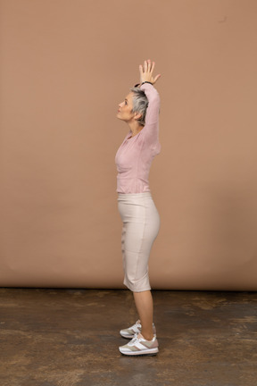 Vista lateral de uma mulher com roupas casuais, posando com as mãos acima da cabeça